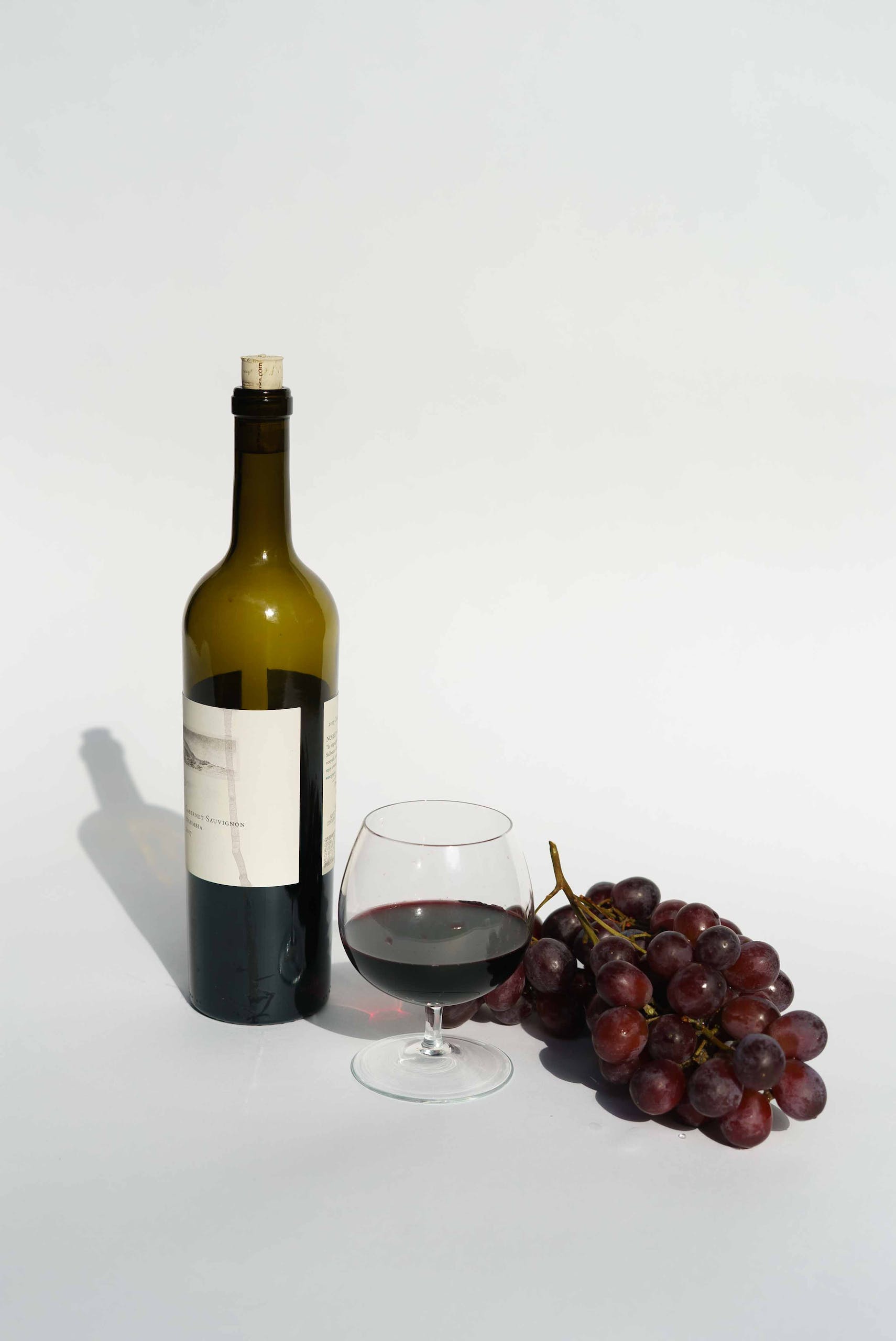 Red Wine Bottle beside a Wine Glass with grapes