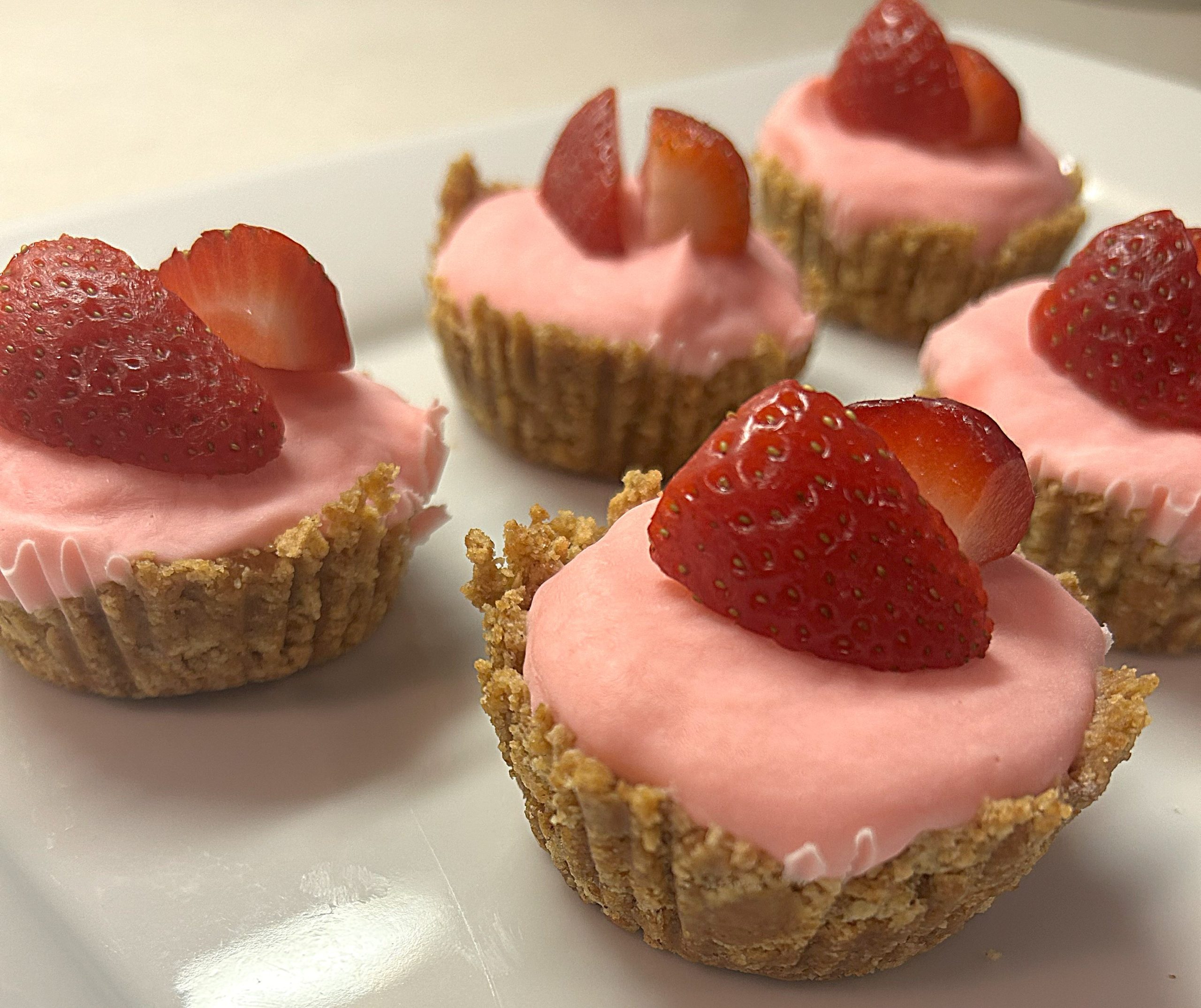 Pink tarts with graham cracker crusts topped with quartered strawberries on a white plate
