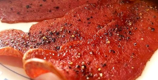 Three strips of turkey bacon with black pepper flakes on a white plate