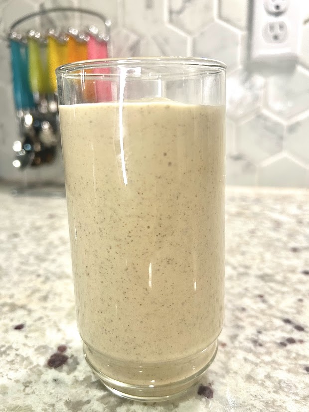 Tan colored complete protein smoothie with chia and chickpeas in a glass container on a granite counter top.