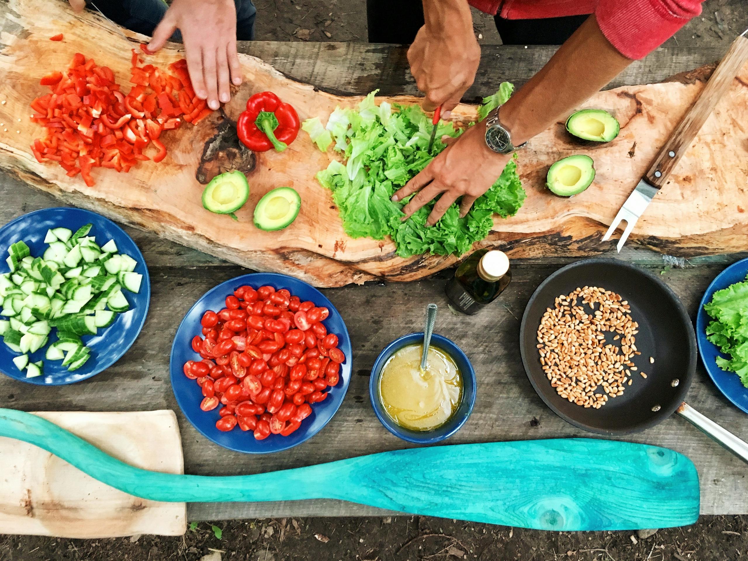 Fresh ingredients for meal prep being prepared on a rustic wooden table, showcasing vibrant vegetables and hands at work.
