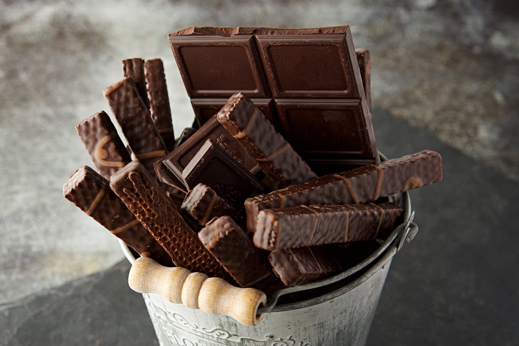 Indulgent assortment of chocolate bars and wafers in a rustic bucket. Perfect for dessert inspiration.